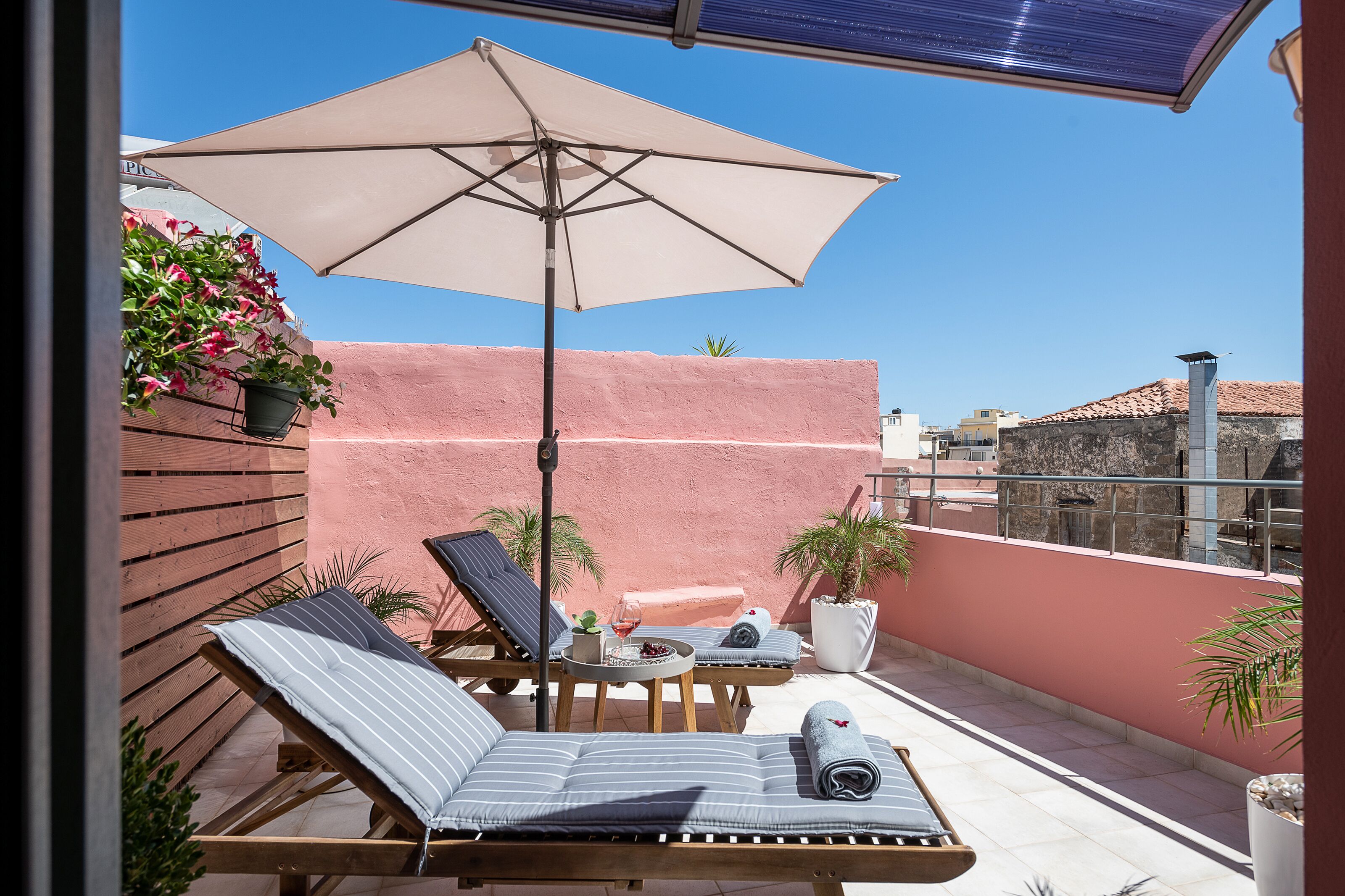 Terraza en la azotea con sillones, una mesa con una bebida, plantas en macetas y un paraguas grande.