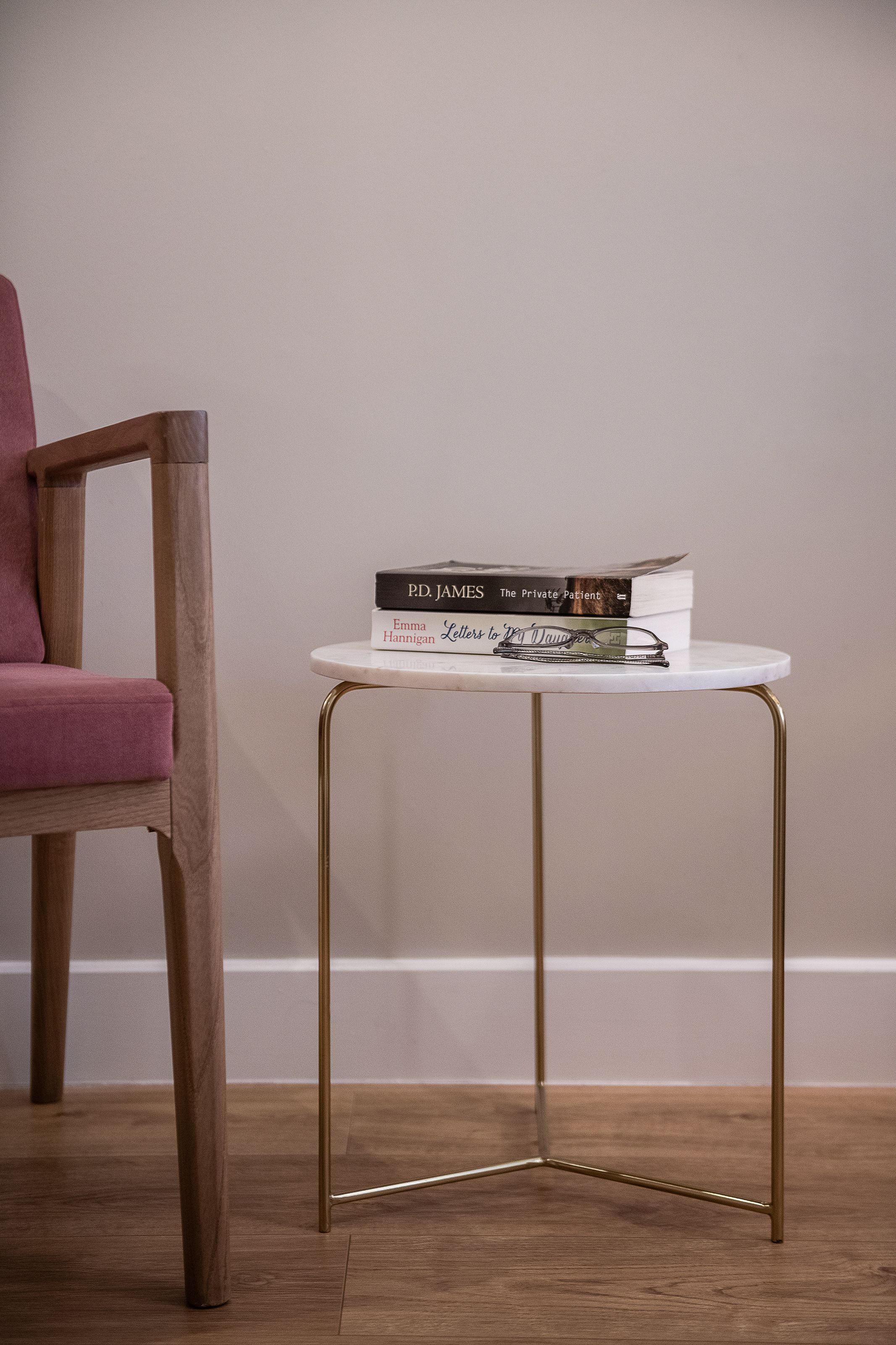 A wooden chair and a small white table with metal legs, holding a stack of books.