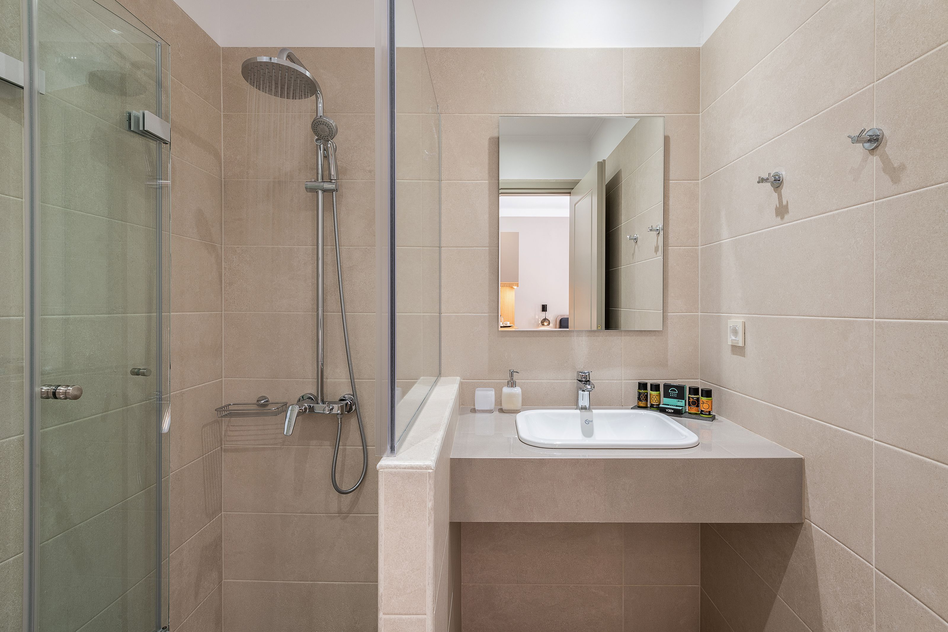 Un bany modern amb boxa de dutxa de vidre, un lavabo amb mirall i paret revestida de rajoles.