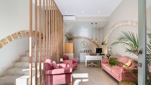 A modern interior with a staircase, pink sofas, a white desk, and a large plant. - Viaggio Elegant Rooms (Chania)
