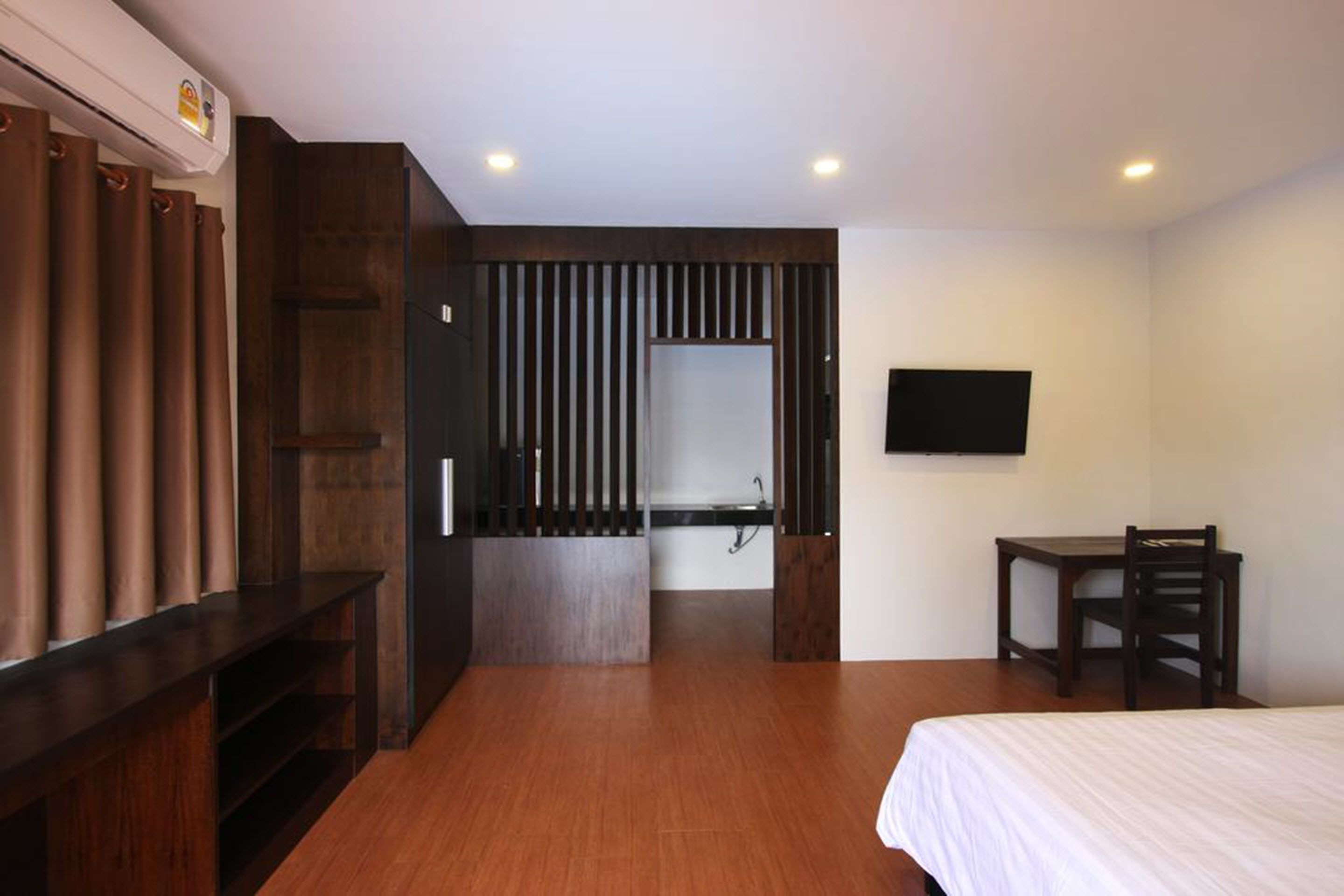 Ein Hotelzimmer mit Holzboden, einem Bett, einem Schreibtisch, einem Sessel, einem an der Wand montierten Fernseher und einem Badezimmer mit Spiegel und Waschbecken.