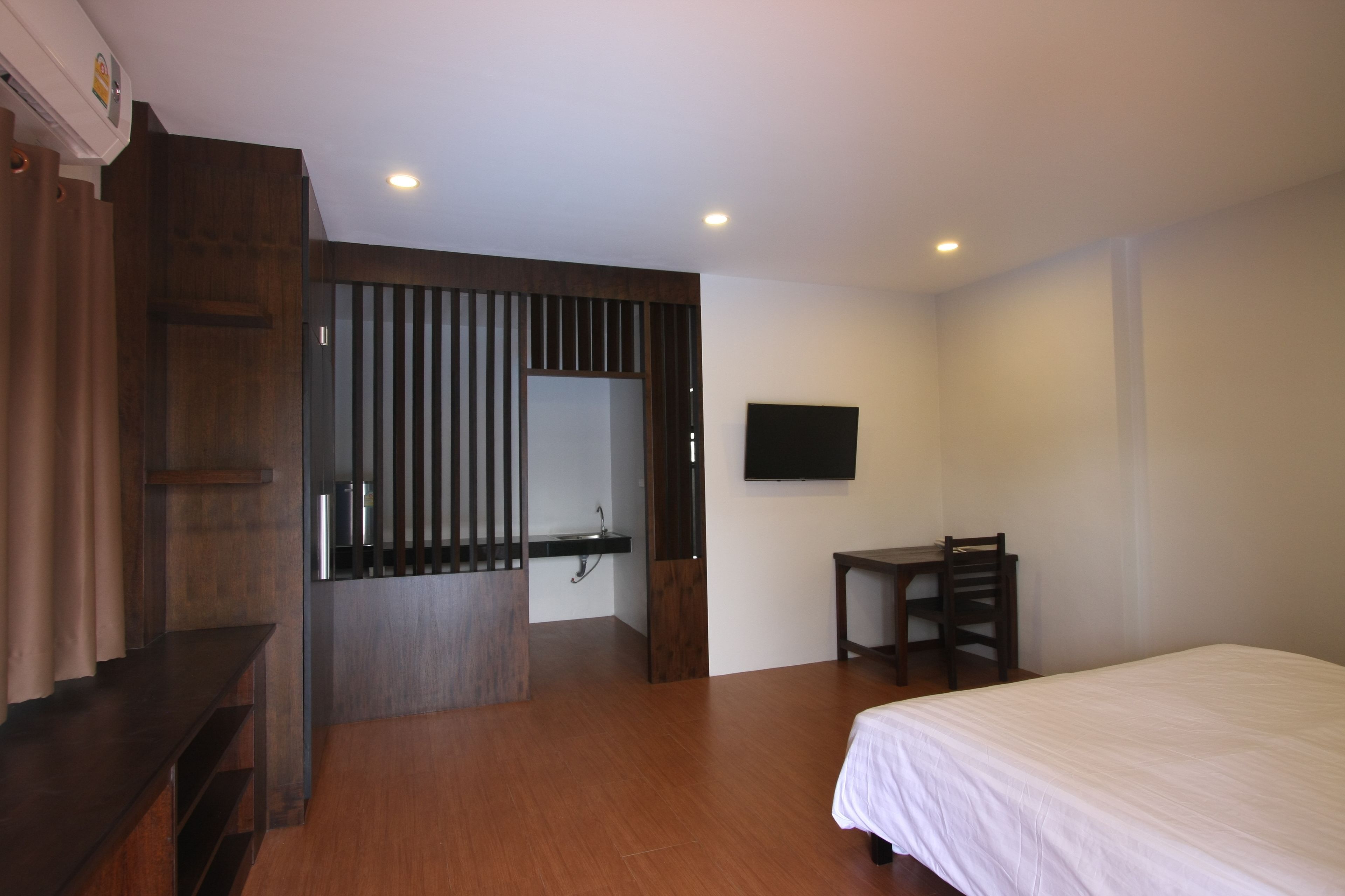 Un dormitorio con cama, escritorio, silla, televisor y baño con espejo y lavamanos.
