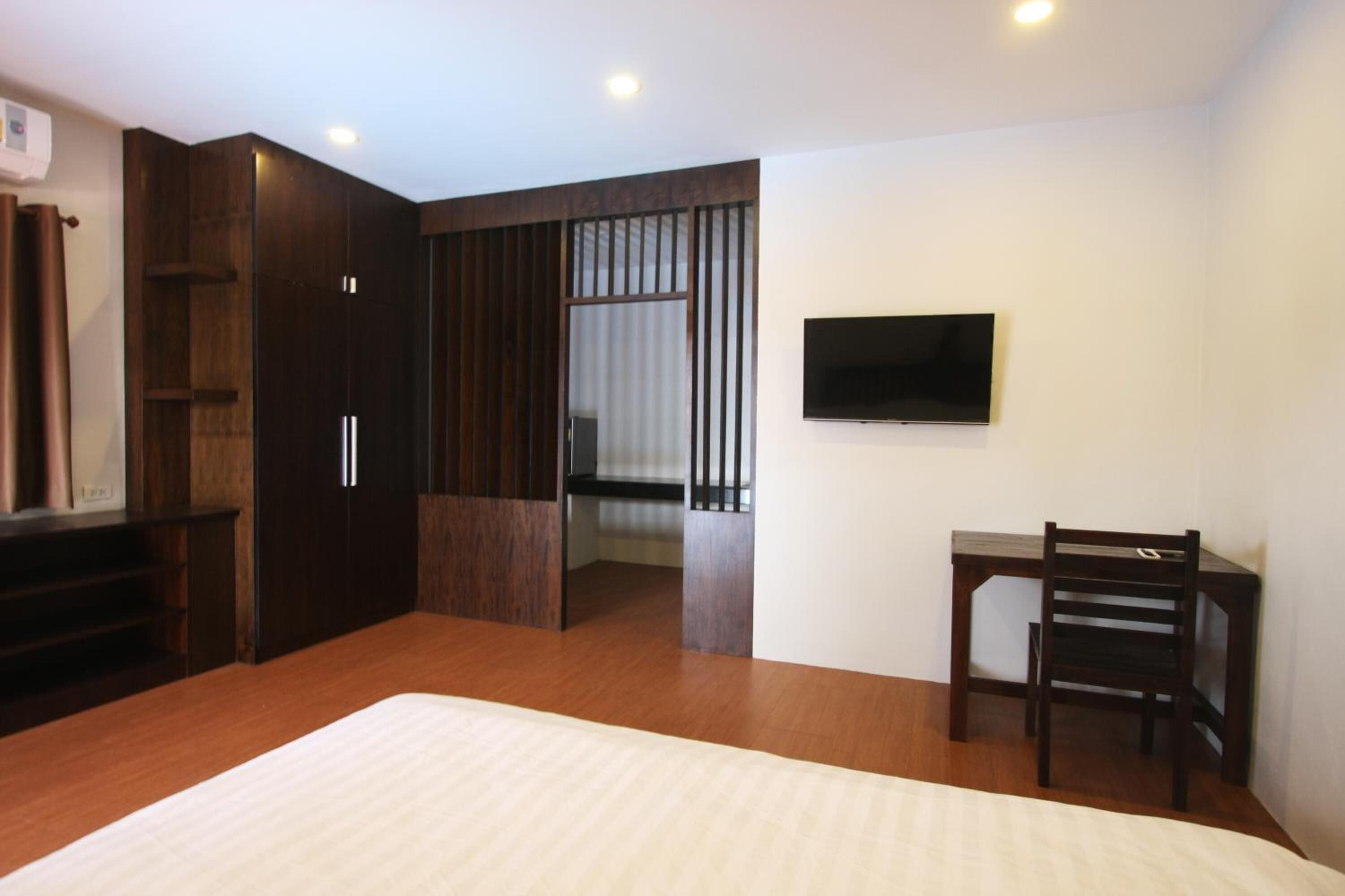 A bedroom with a large bed, a TV mounted on the wall, a desk with a chair, and a wardrobe.