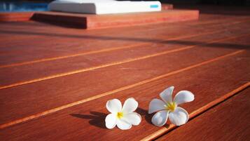 Una terraza de madera con dos flores blancas y un objeto blanco al fondo.