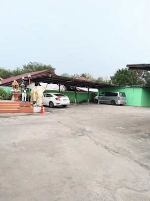 Un espace de stationnement avec deux voitures, un petit sanctuaire et un bâtiment vert.