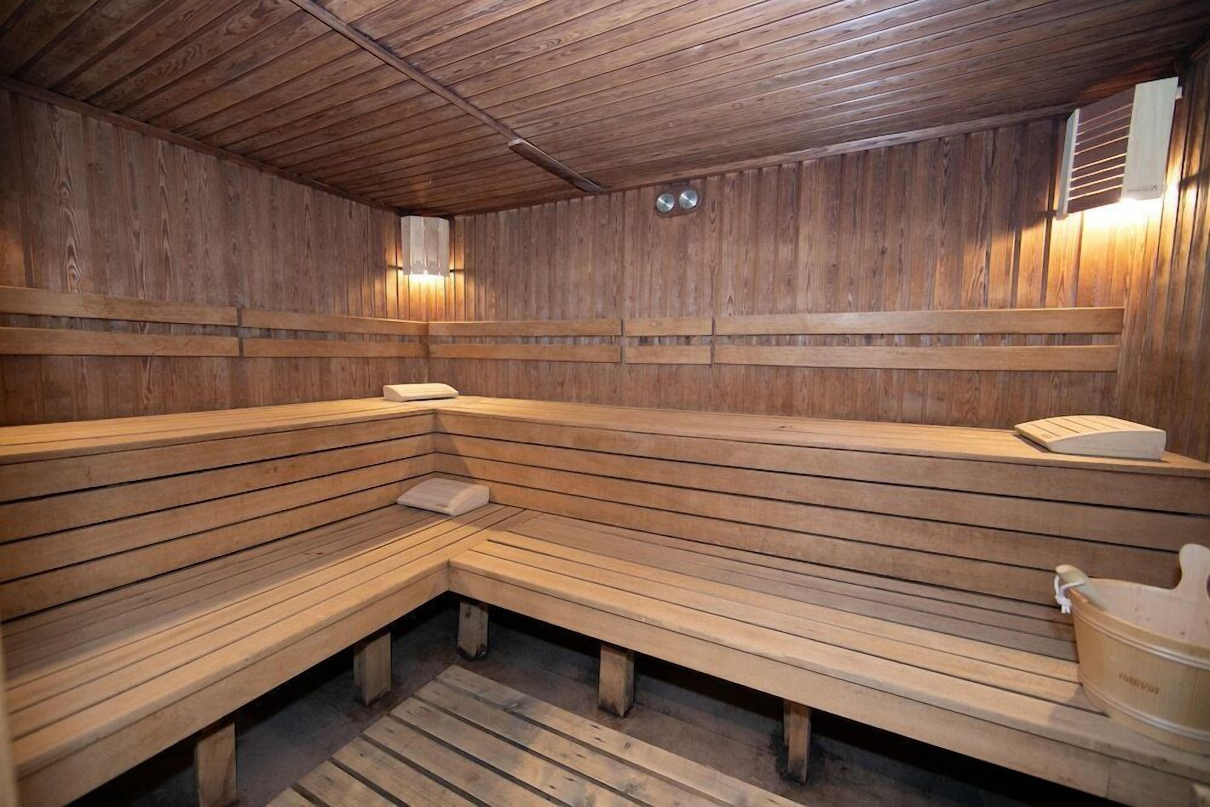 A sauna room with wooden benches and benches, a wooden floor, and a wooden wall with a light fixture.