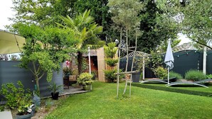 Un jardin bien entretenu, agrémenté de diverses plantes, d’une structure en bois et d’un banc incurvé en métal blanc.