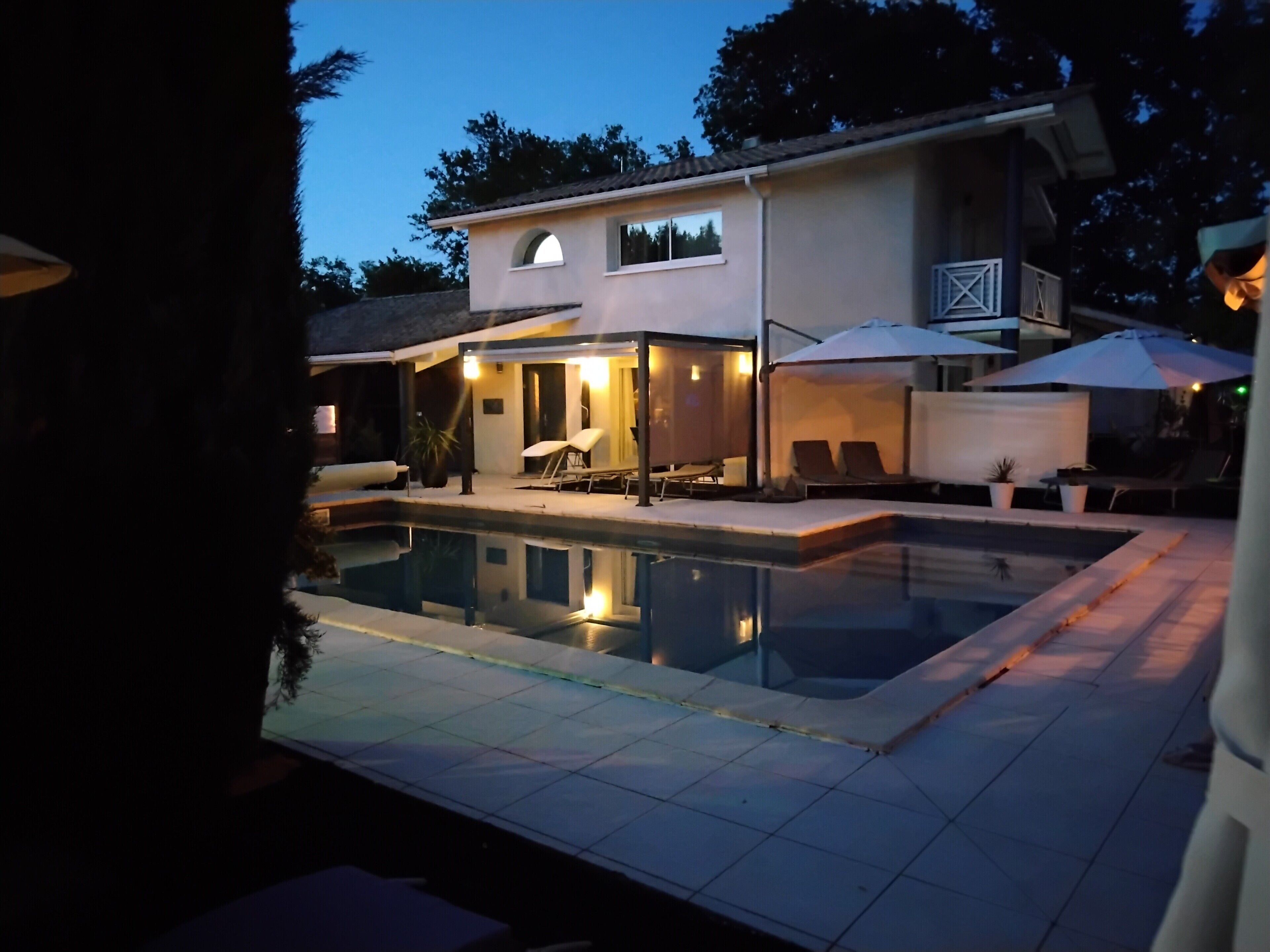 Una casa moderna con piscina, mobiliario de exterior y un patio cubierto.