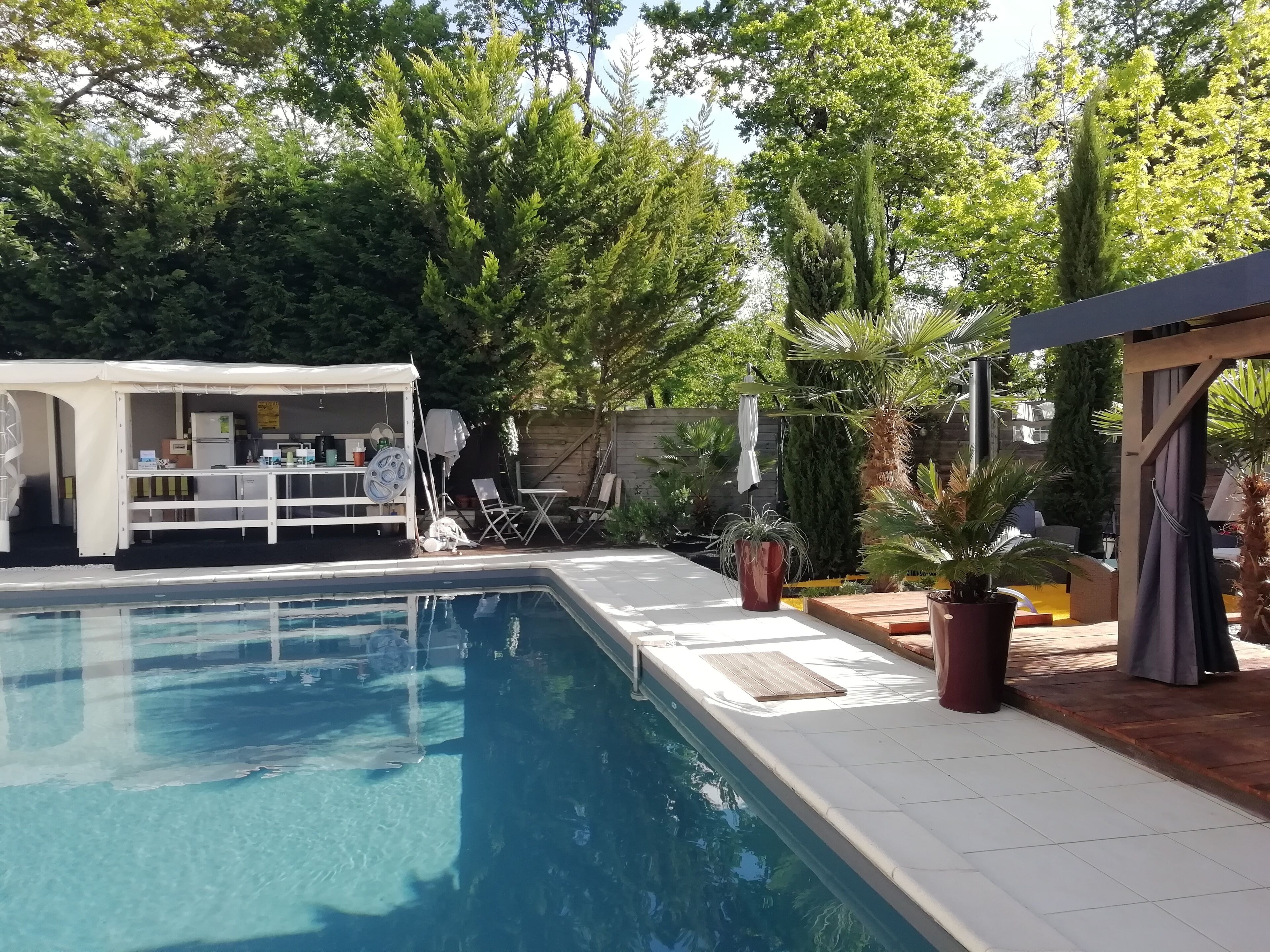 A swimming pool with a covered patio area, outdoor furniture, and a small structure with a table and chairs.