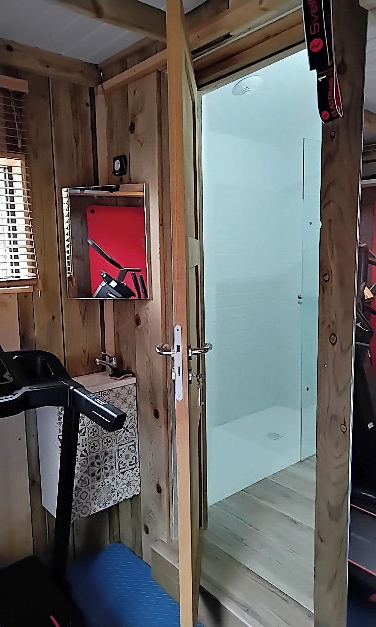 Een houten interieur met een douche, een klein wastafeltje en een spiegel.
