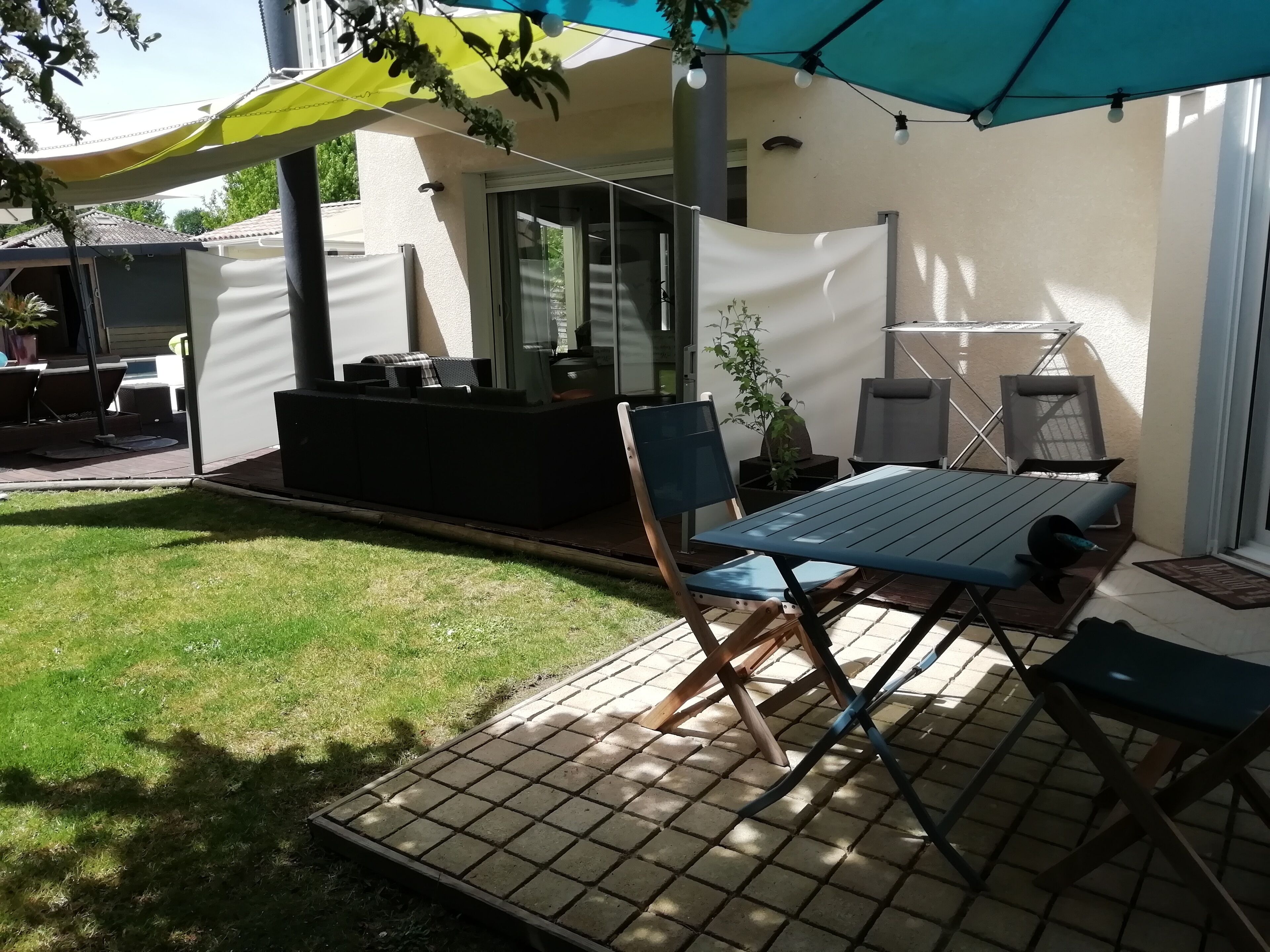 Een buitenpatio met een tafel en stoelen, een klein zithoekje en een overdeeld gedeelte met een plant.