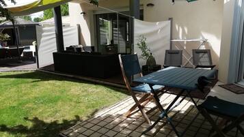 Een buitenpatio met een tafel en stoelen, een klein zithoekje en een overdeeld gedeelte met een plant.