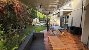 Een buitenpatio met een houten terras, een ingebouwde plantenbak en een tafel met stoelen.