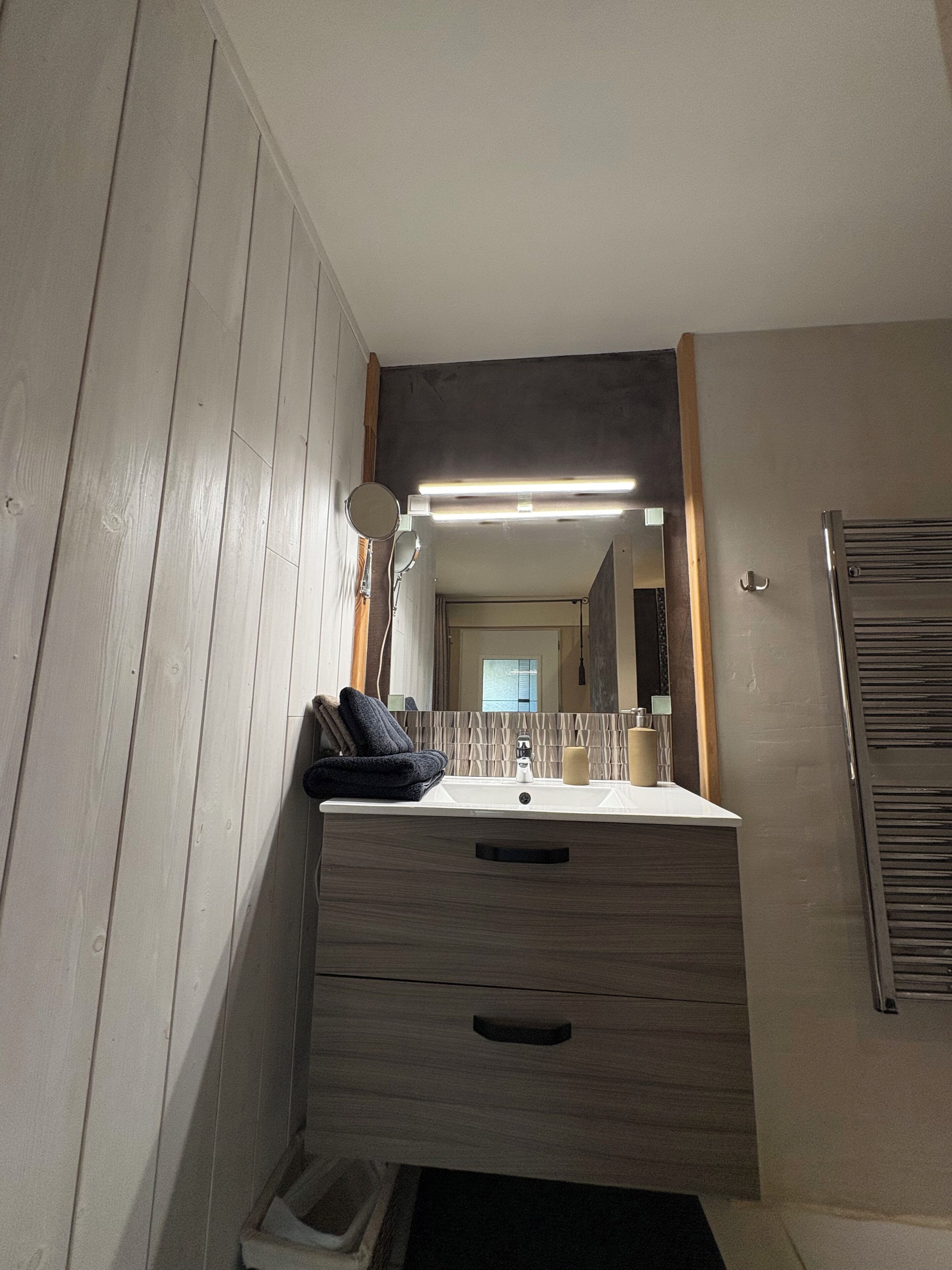 Un baño con tocador de madera, un espejo, un lavamanos y un perchero para toallas.