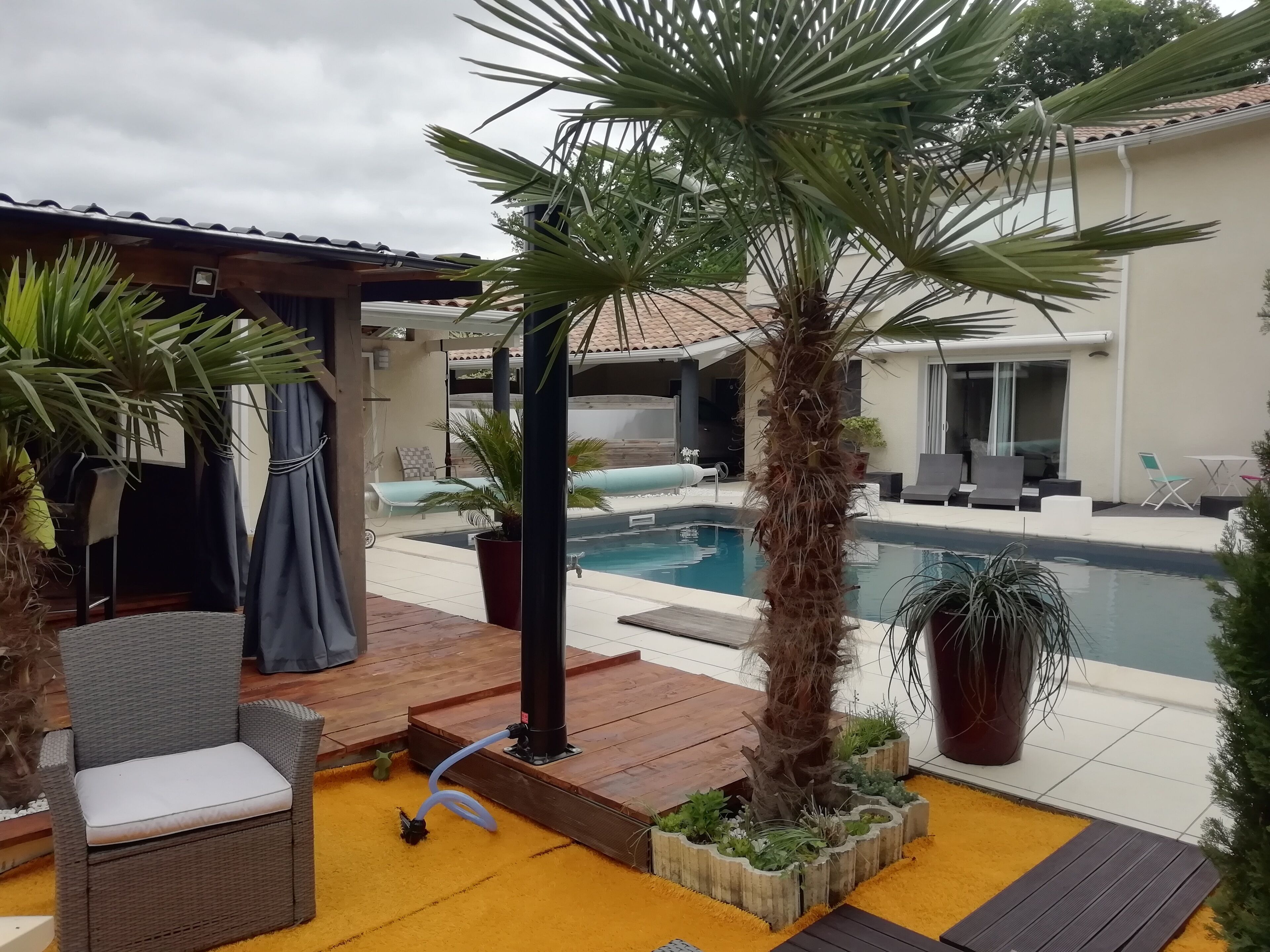 Un área junto a la piscina con una terraza de madera, una silla de descanso, una mesita y una planta en maceta.