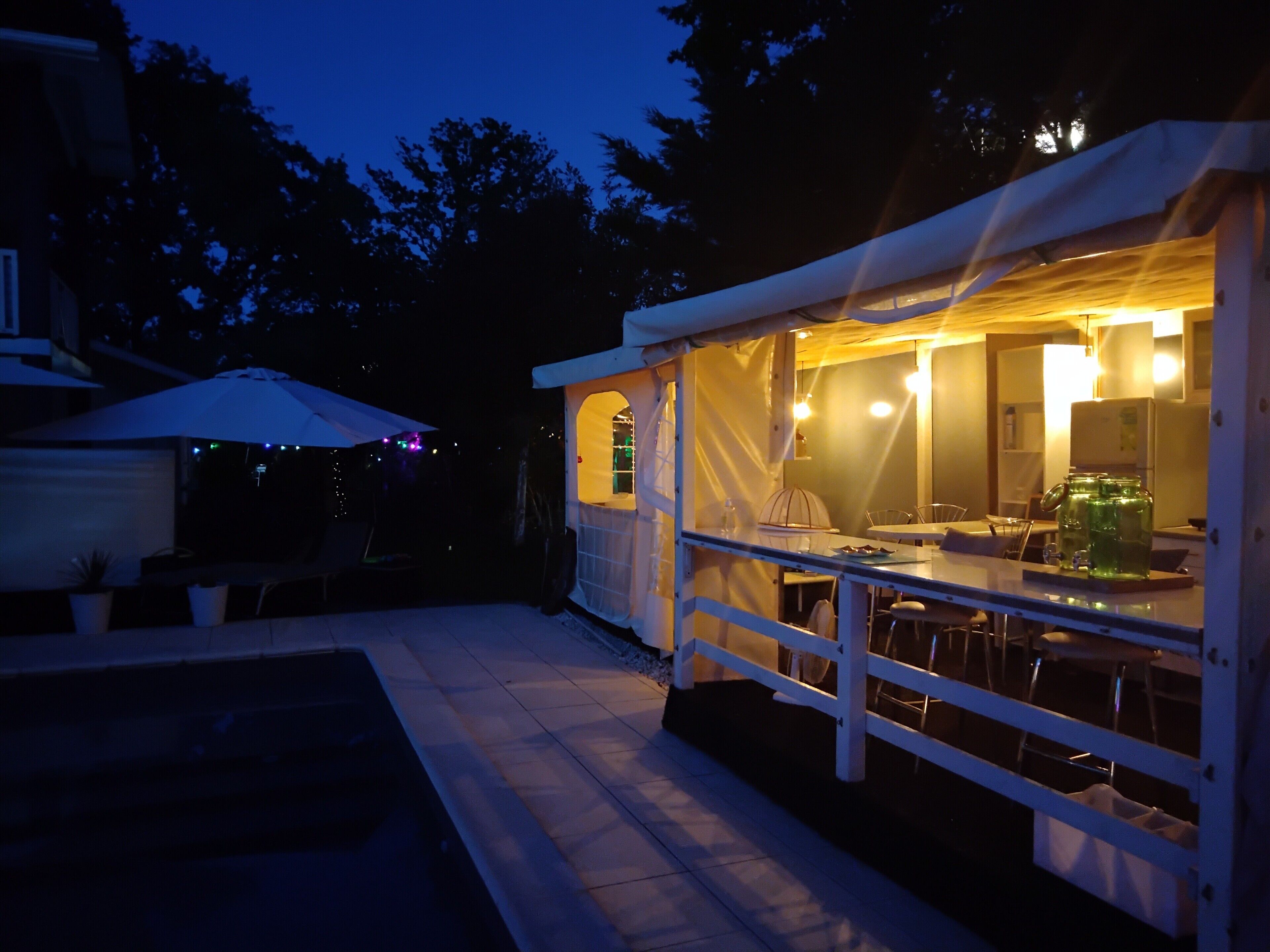 A covered outdoor dining area with a pool, a white fence, and a table with chairs.