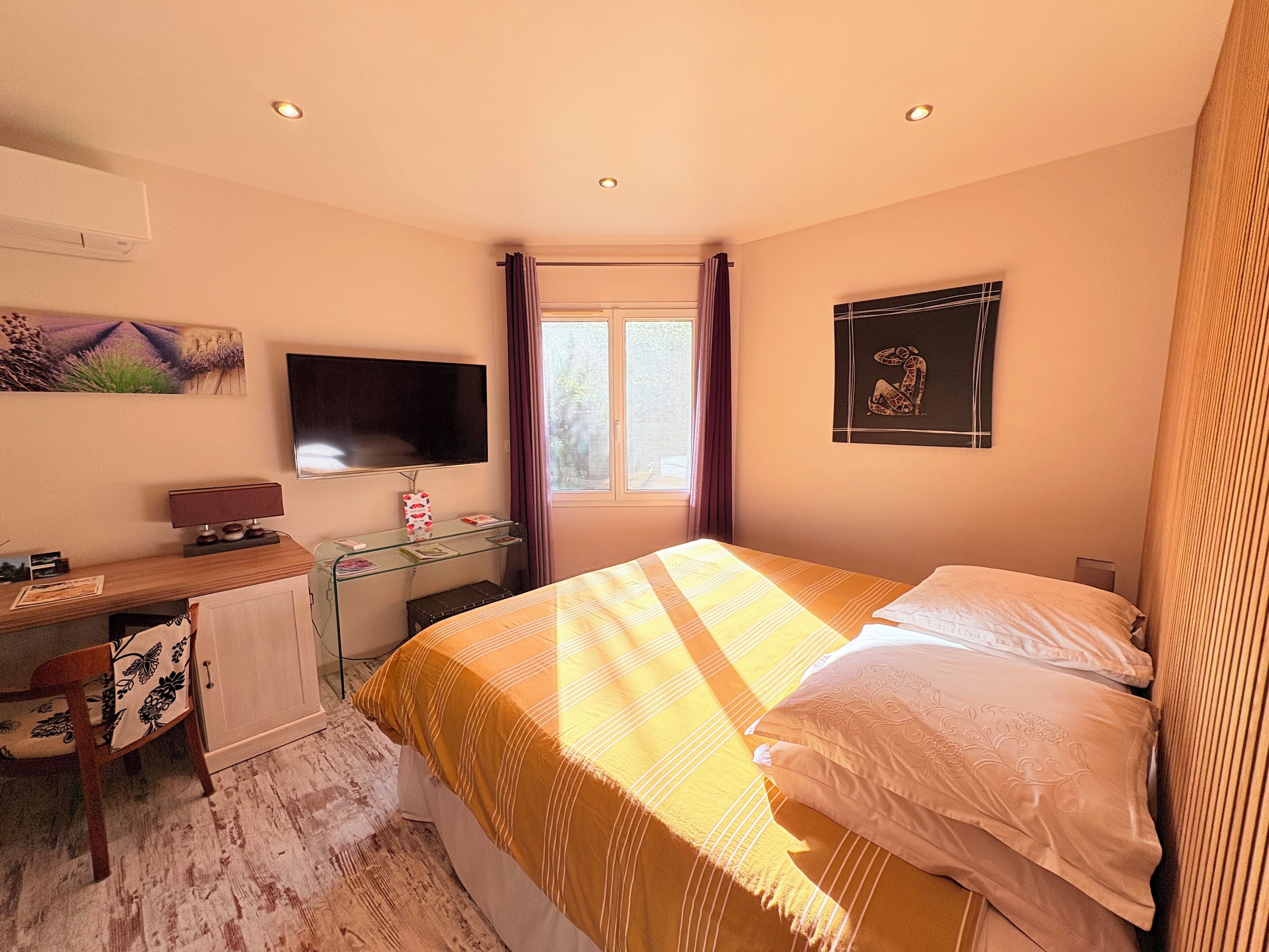 Un dormitorio con una cama, un escritorio con computadora, un televisor y una ventana con cortinas.