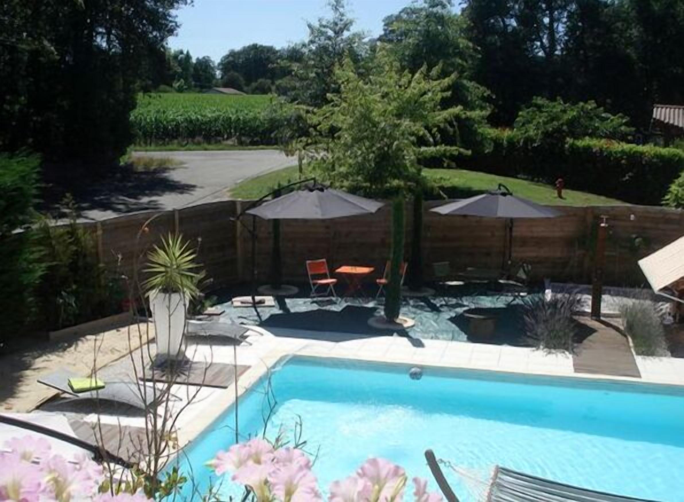 A backyard with a swimming pool, wooden deck, and outdoor furniture.