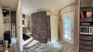 Une chambre d’hôtel compacte dotée d’une douche à parois incurvées, d’un four à micro-ondes intégré et d’une bibliothèque remplie de livres.