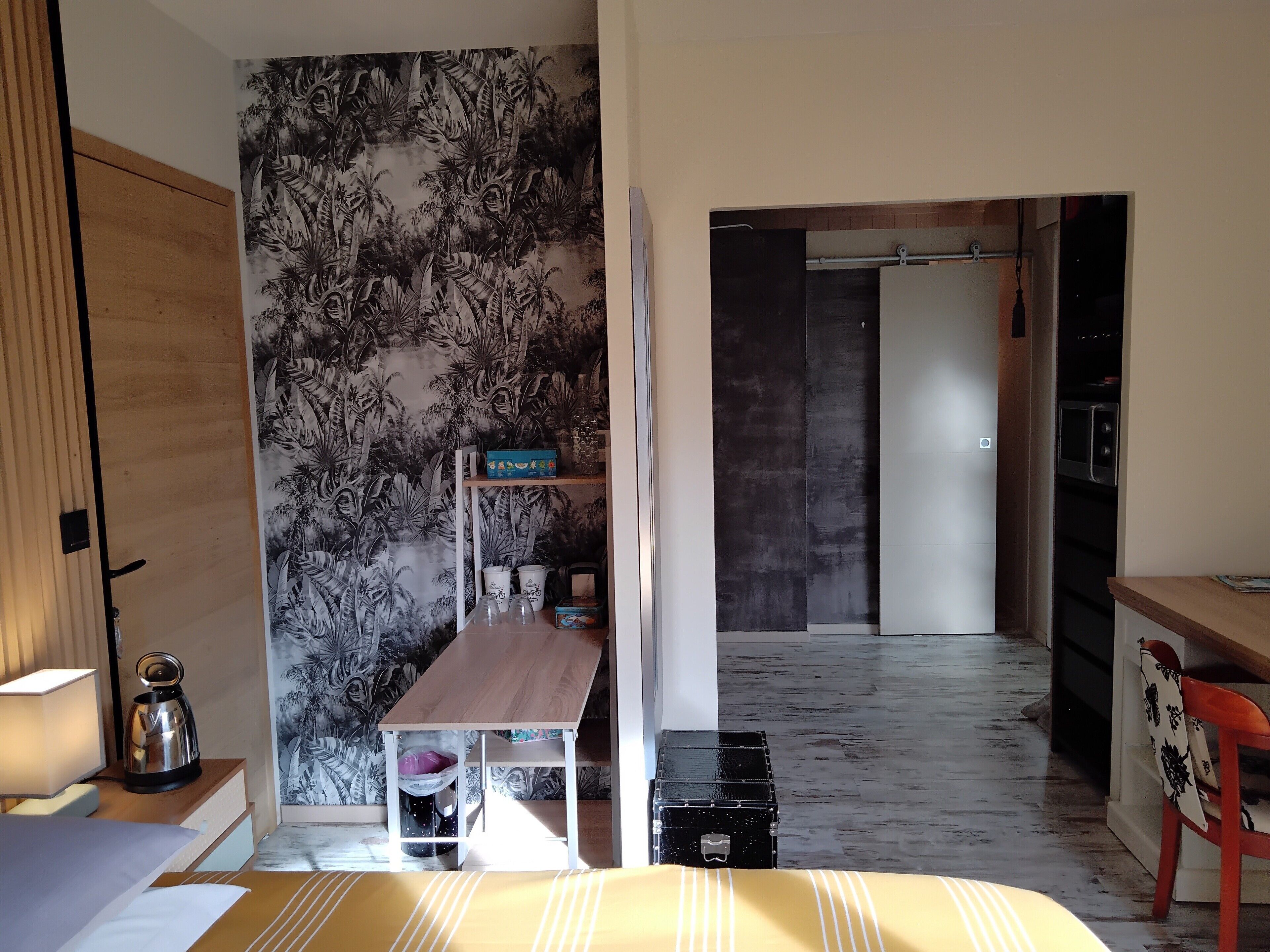 Een moderne kamer met een bed, een bureau, een koffiezetapparaat en een plank met keukenbenodigdheden.