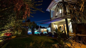 Une maison moderne dotée d’une piscine, d’un espace salon extérieur et d’un jardin bien éclairé la nuit.