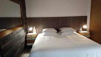 A bedroom with a wooden headboard, a large bed with white bedding, two bedside tables with lamps, and a wooden wardrobe.