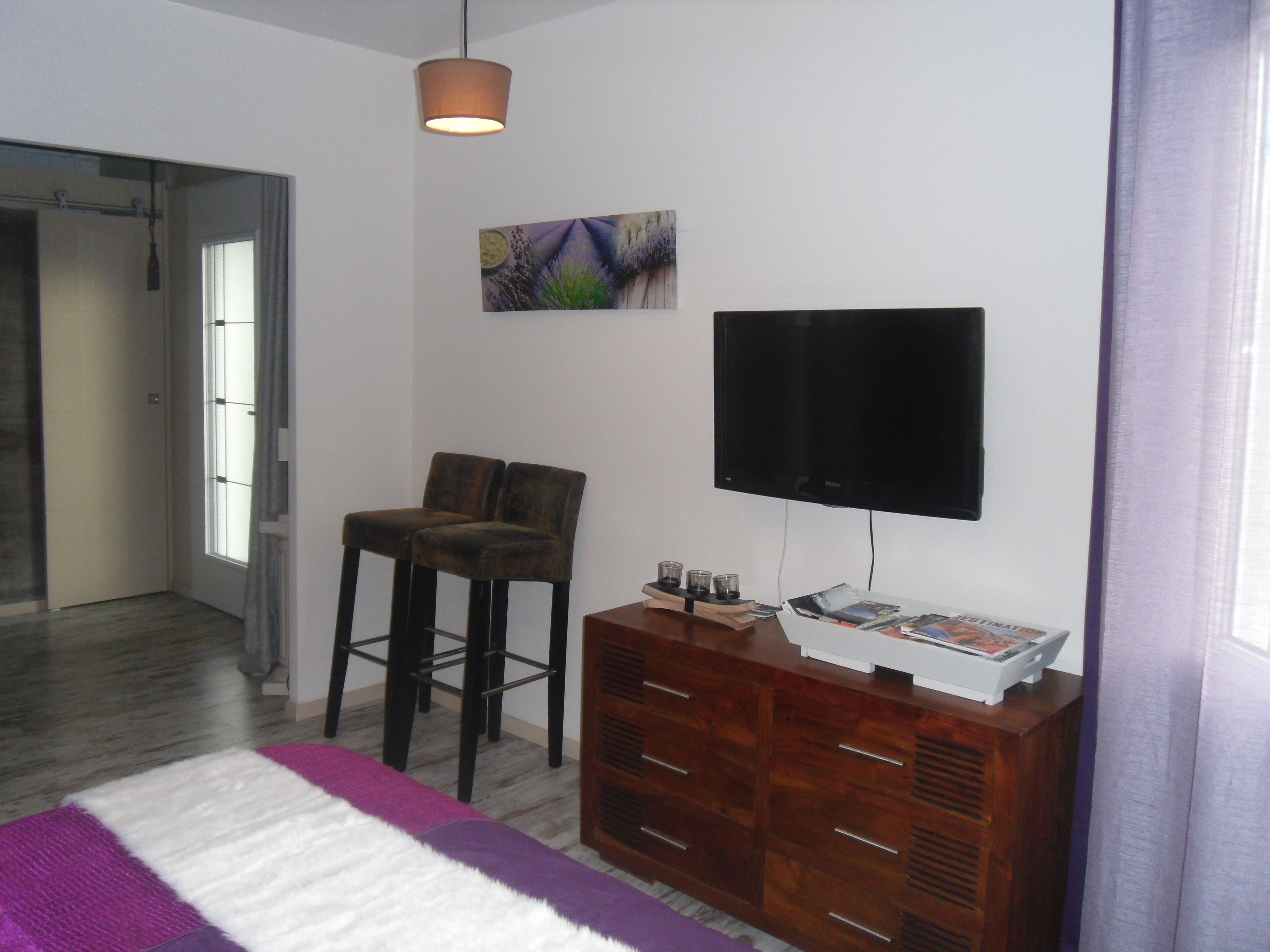 Un dormitorio moderno con cama, televisor, cómoda de madera y un cuadro en la pared.