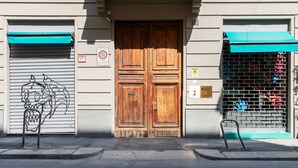 A double wooden door with a metal plaque, a metal gate with a green awning, and a metal chair in front of a building with a garage door. - easyhomes - Brera Luxury Suites (Milan)