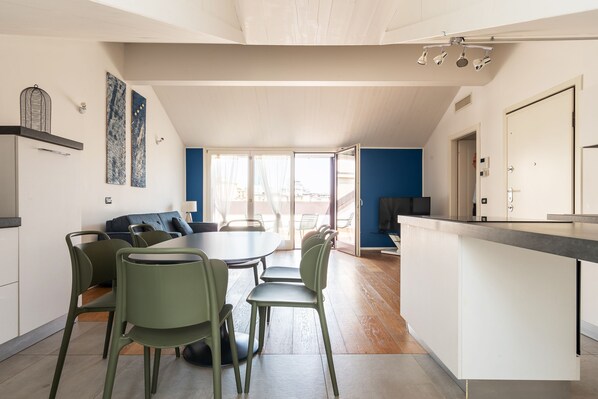 A modern kitchen with a dining area, featuring a large island, green chairs, and a view to the outside. - easyhomes - Brera Luxury Suites (Milan)