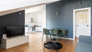 A modern living room with a flat-screen TV on a white cabinet, green chairs around a dining table, and a grey sofa. - easyhomes - Brera Luxury Suites (Milan)