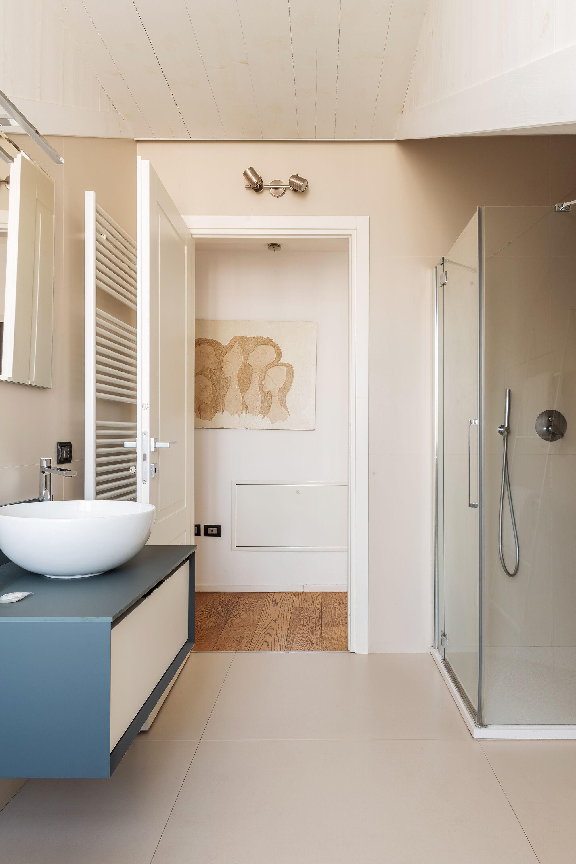 A modern bathroom with a white sink, a glass shower enclosure, and a wooden floor.