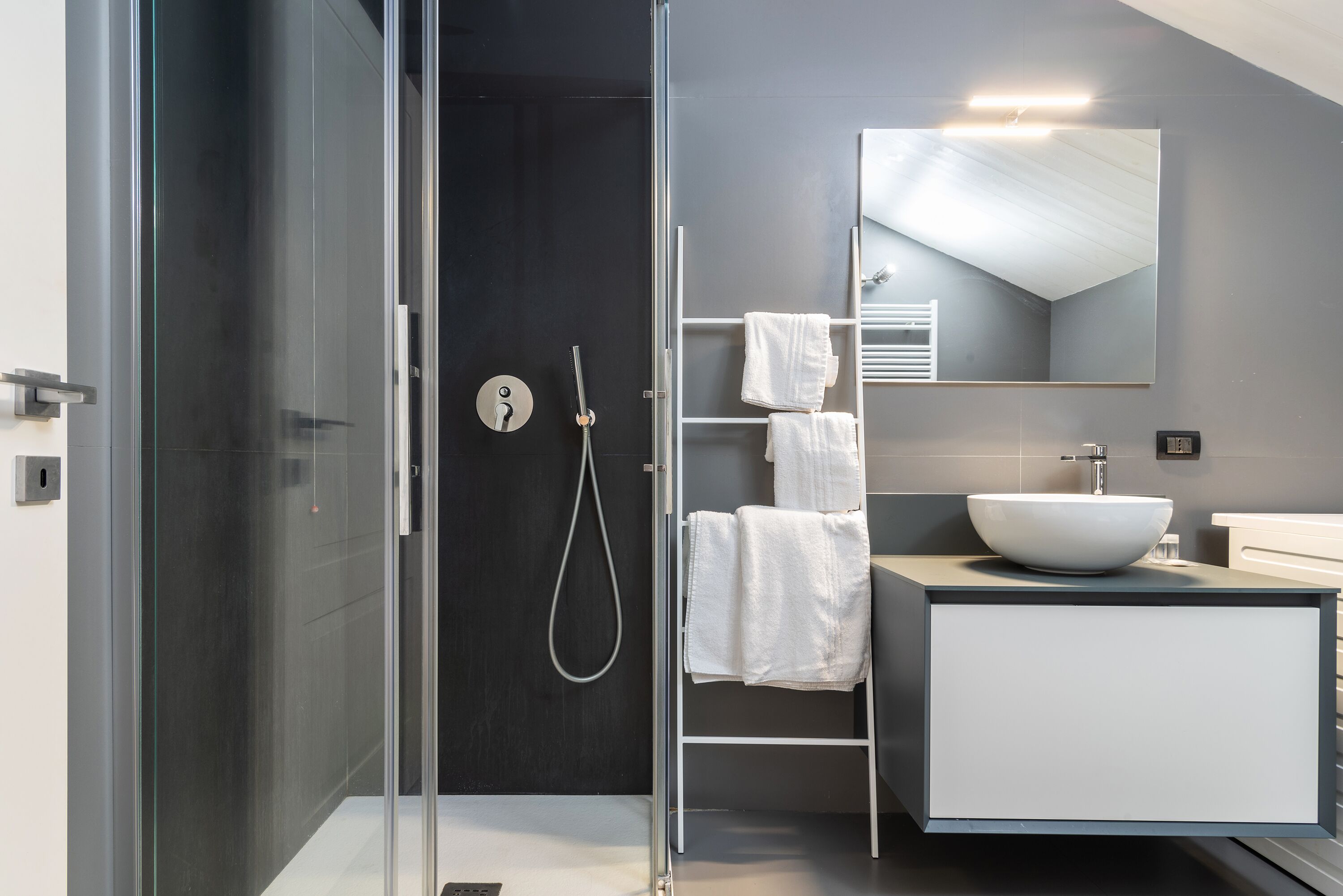 Un bany modern amb dutxa d'ús de vidre, un lavabo blanc i un suport per tovalloles.