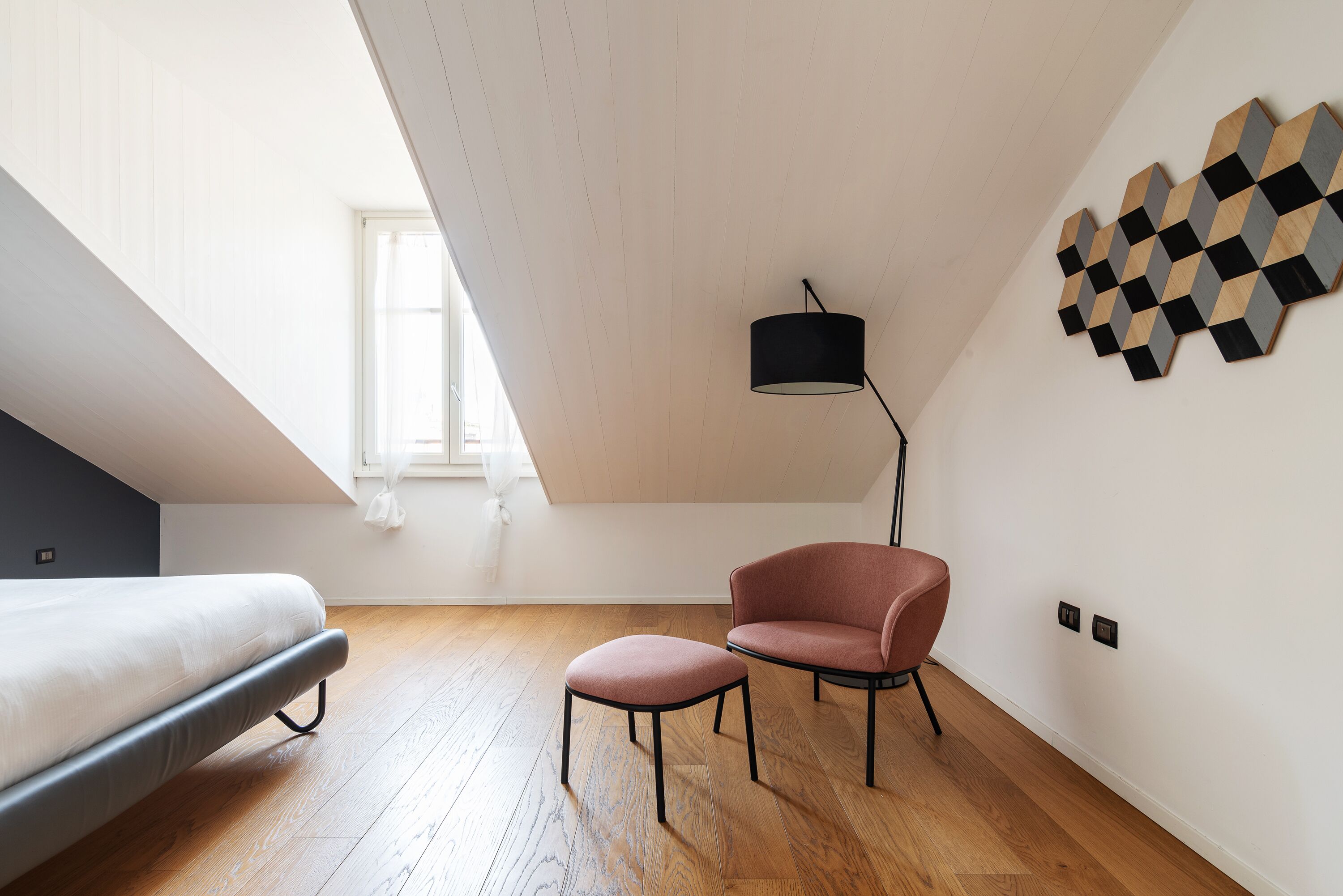 Une chambre à coucher moderne avec un lit, une chaise, une lampe et une œuvre d’art géométrique accrochée au mur.