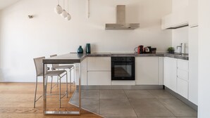 A modern kitchen with white cabinetry, a built-in oven, and a dining area with a metal table and chairs. - easyhomes - Brera Luxury Suites (Milan)