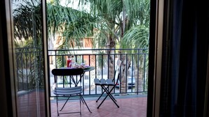 Un balcon avec une table et des chaises, une vue sur des palmiers et un sol carrelé.