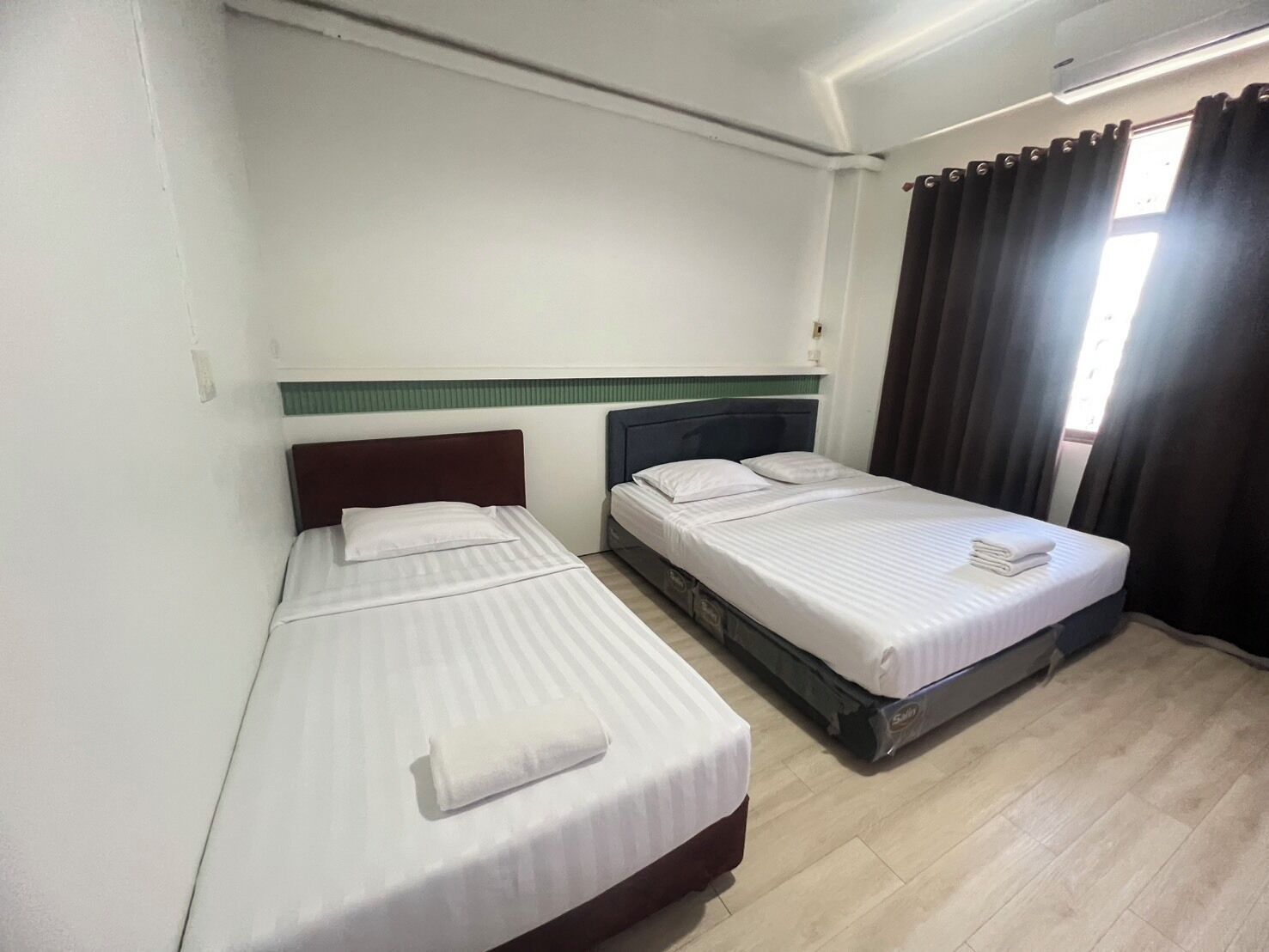 A room with two beds, a window with curtains, and a light switch on the wall.