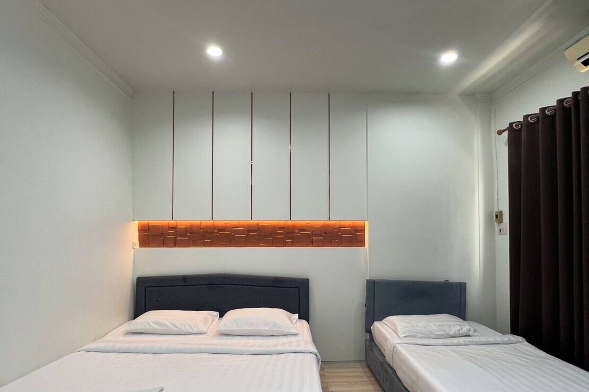 Habitación de hotel con dos camas, cabecero de madera, luz de techo y ventana con cortinas.