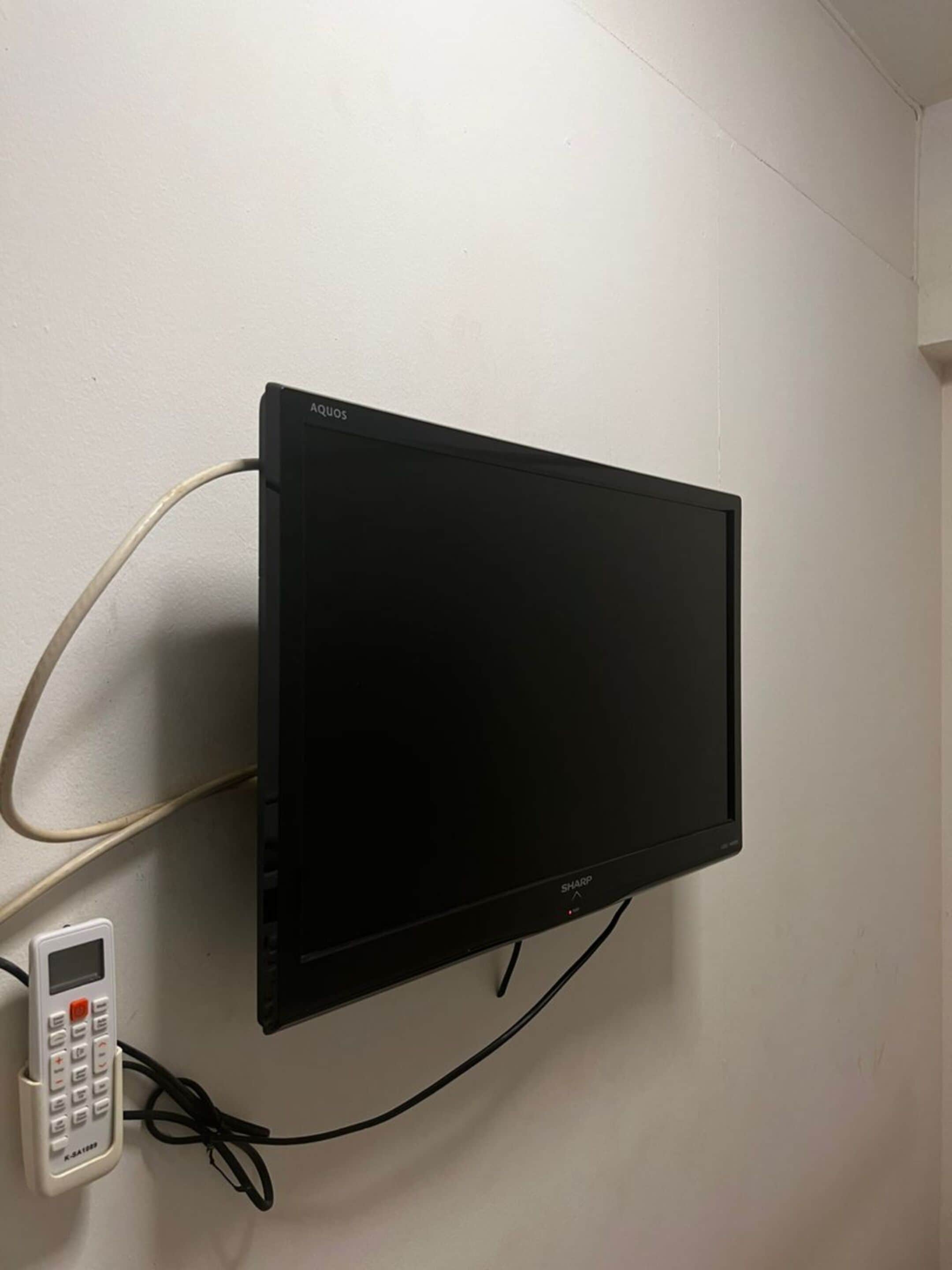 Et fladskærms-tv ophængt på væggen med en fjernbetjening og et kabel tilsluttet.