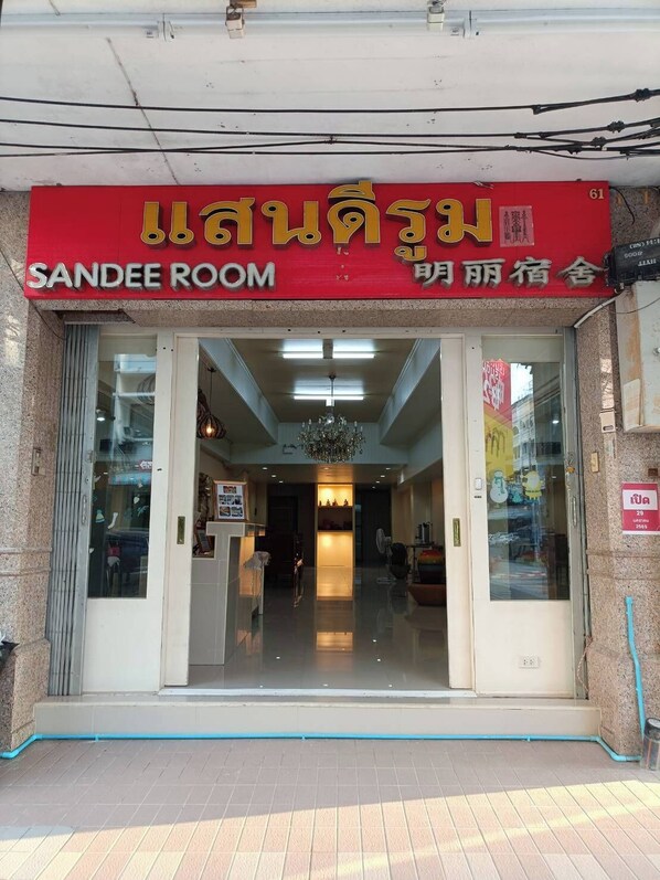 La entrada de un hotel con un letrero rojo que dice "SANDEE ROOM" y otro letrero en un idioma diferente.