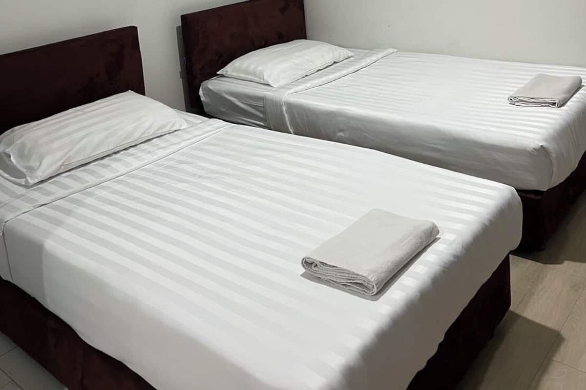 Habitación de hotel con dos camas individuales, cabecero de madera, pared blanca y aire acondicionado instalado en el techo.