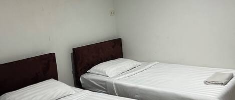 Une chambre d’hôtel avec deux lits simples, une tête de lit en bois, un mur blanc et un appareil de climatisation fixé au plafond.