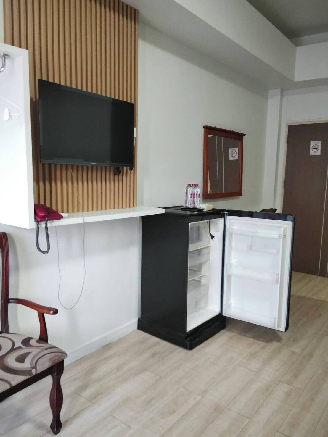 A compact kitchenette with a built-in TV, a small fridge, and a wooden panel wall.