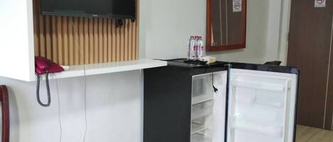 Una kitchenette compacta con una TV integrada, un refrigerador pequeño y un revestimiento de pared de madera.