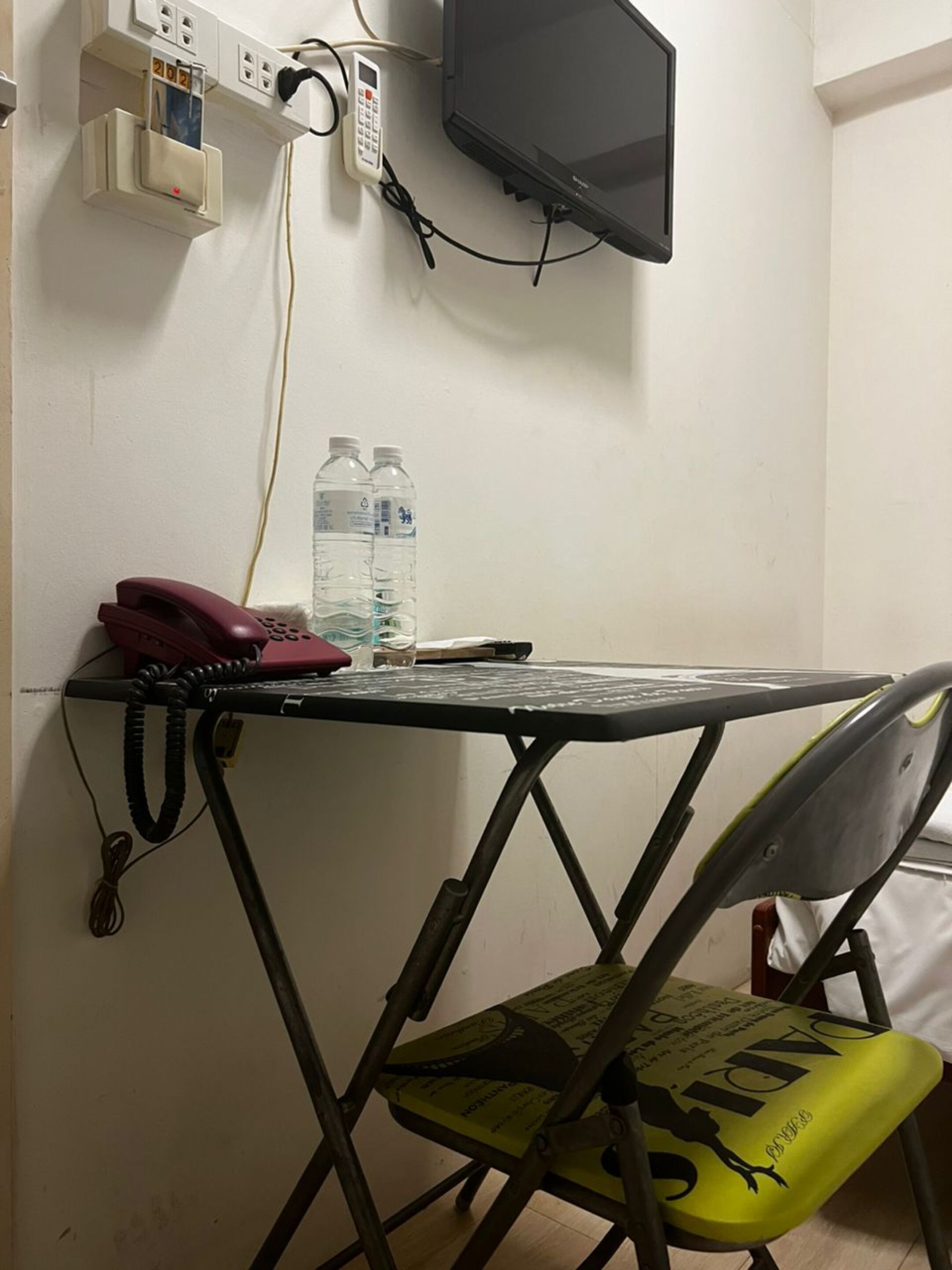 Ένας μικρός χώρος εργασίας με ένα γραφείο, μια καρέκλα, ένα τηλέφωνο και ένα μπουκάλι νερό.