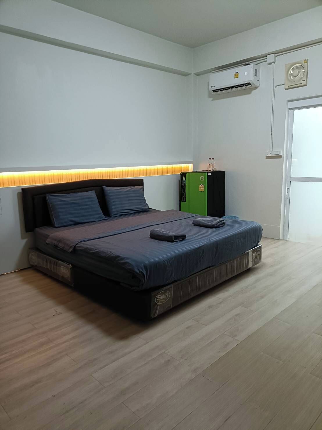 Ein Schlafzimmer mit einem Bett, einem Kopfteil mit integrierter Beleuchtung, einer Klimaanlage und einem grünen Schrank.