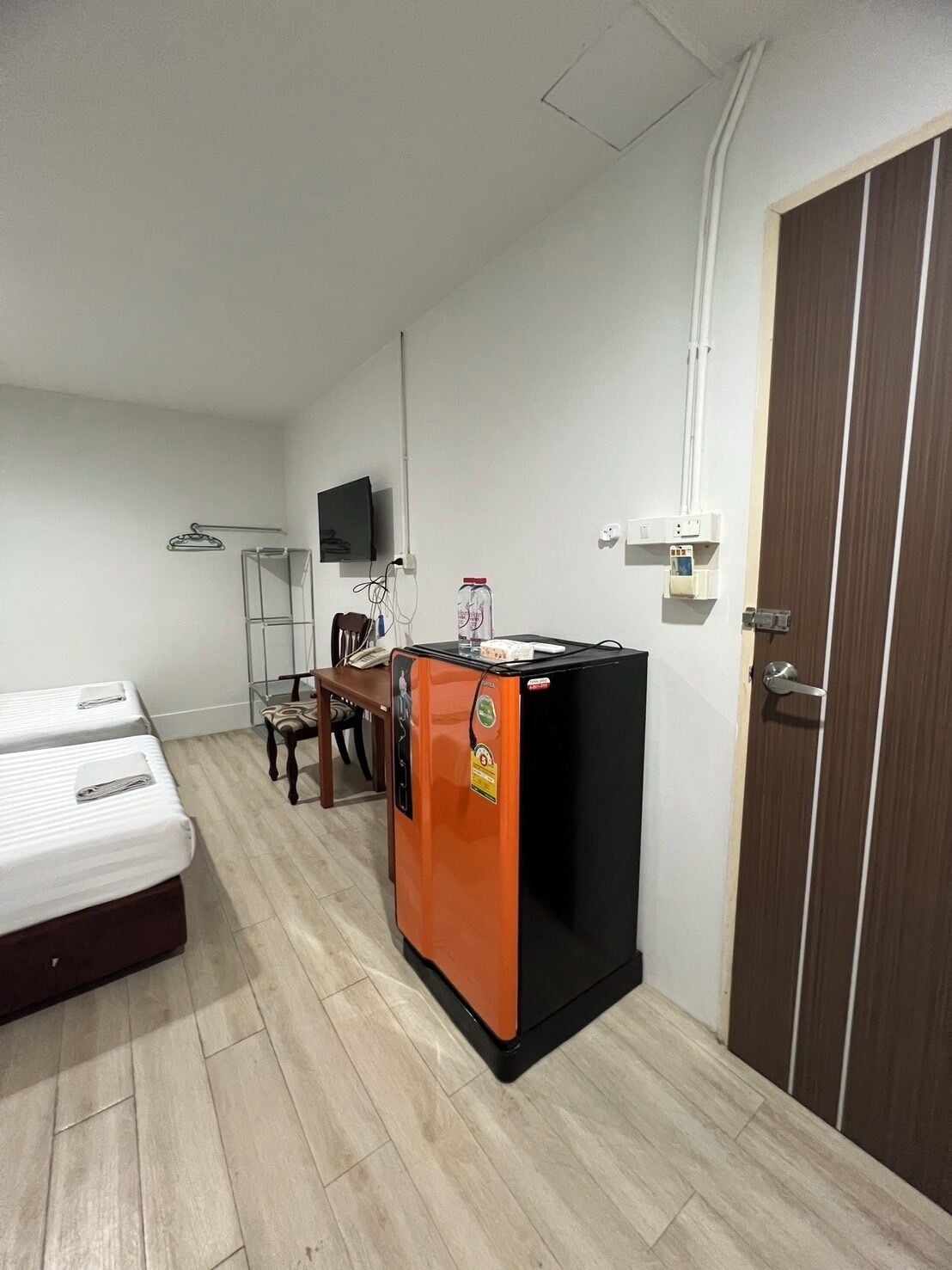 Una camera d'albergo compatta con un letto, una piccola scrivania, un frigorifero e una televisione a parete.