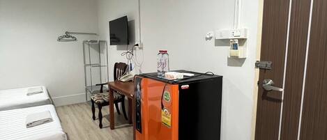 A compact hotel room with a bed, a small desk, a refrigerator, and a television mounted on the wall.