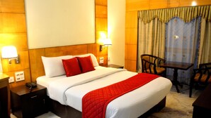 A hotel room with a large bed, a desk, and two chairs. There are two wall-mounted lamps and a telephone on the nightstand. - Hotel City Centaur (Bengaluru)