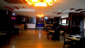 A restaurant interior with wooden flooring, tables, chairs, and a central chandelier. - Hotel City Centaur (Bengaluru)