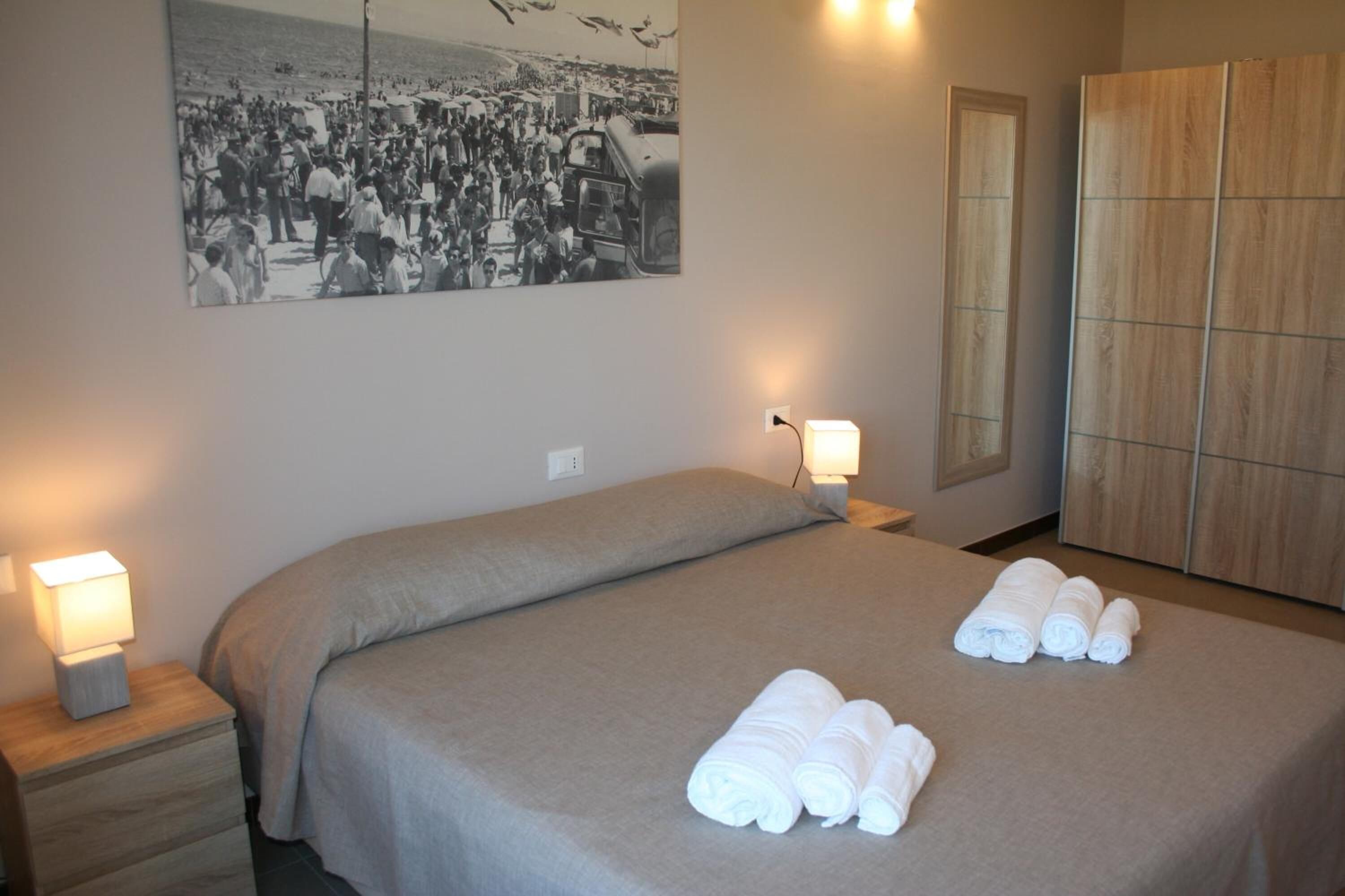 A hotel room with a bed, two bedside lamps, a large poster on the wall, and a wardrobe.